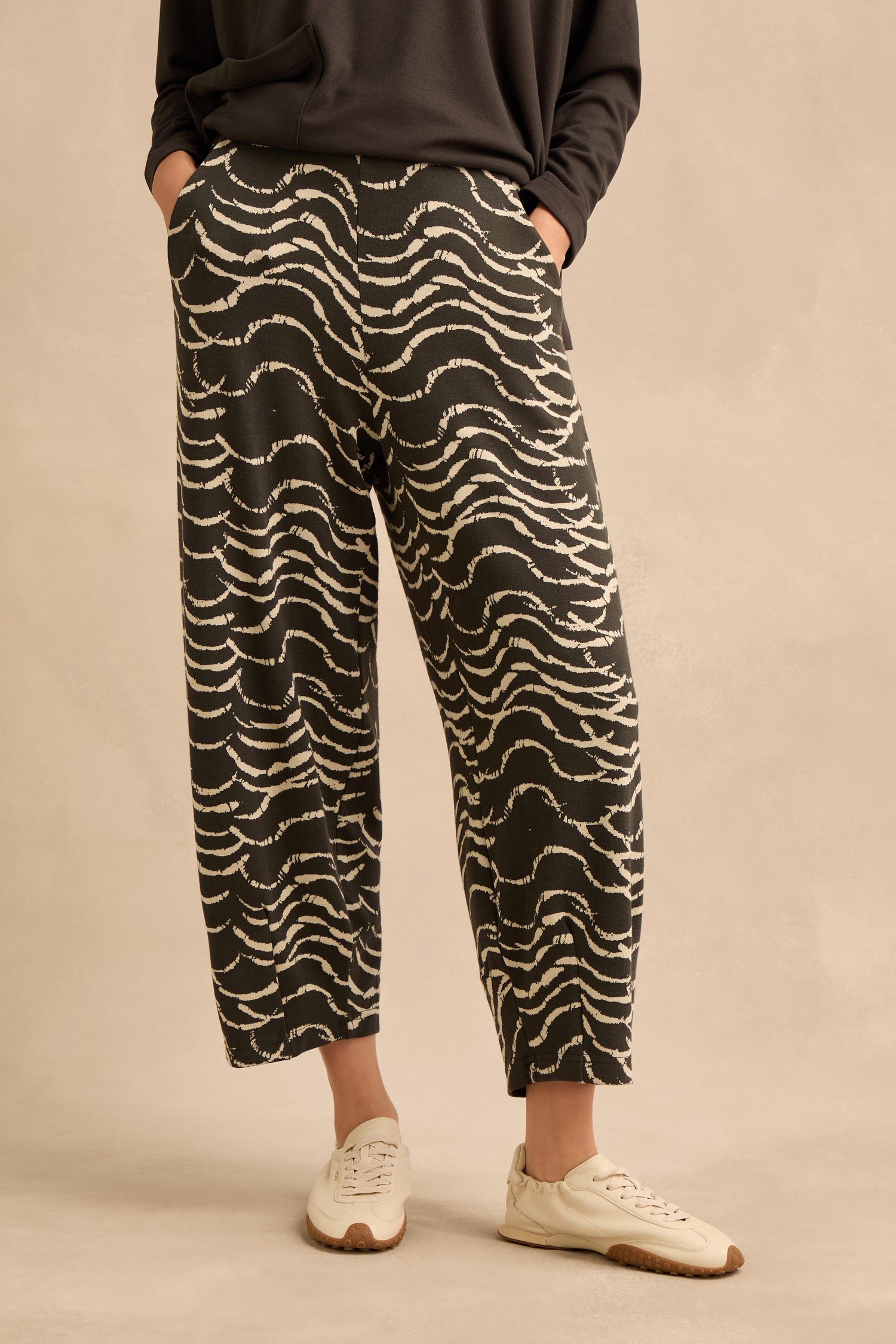 A person is wearing the Dancing Waves Jersey Bubble Trousers in stretch jacquard with a dark top and white sneakers, standing against a beige background.