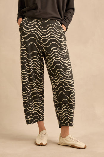 A person is wearing the Dancing Waves Jersey Bubble Trousers in stretch jacquard with a dark top and white sneakers, standing against a beige background.