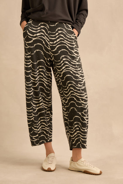 A person is wearing the Dancing Waves Jersey Bubble Trousers in stretch jacquard with a dark top and white sneakers, standing against a beige background.