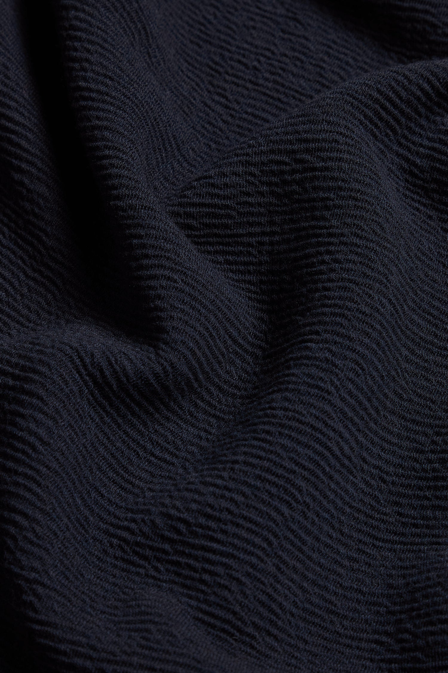 Close-up of dark, textured fabric with visible ridges and folds, highlighting the distinctive surface pattern and unique finish of the Double Jersey Crinkle Trousers.