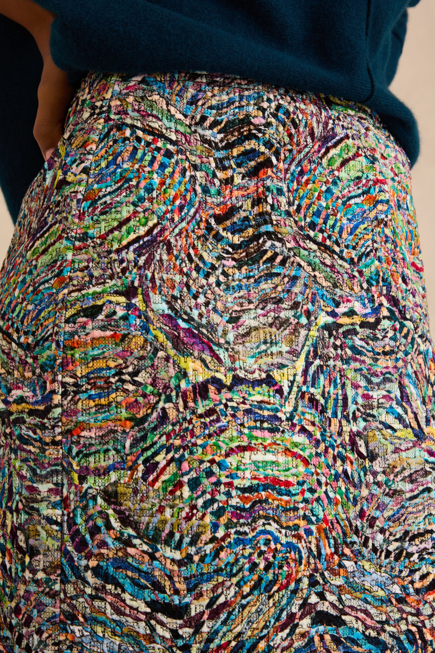 Close-up of a person wearing a dark green top and the Patchwork Fields Jersey Tube Skirt, a multicolored, textured jacquard jersey midi skirt featuring an intricate, abstract pattern.