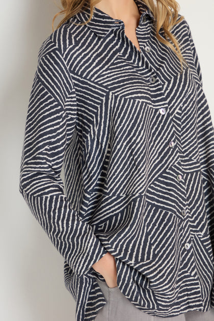 Model wearing the Linear Prism Shirt, a black and white striped geometric print, long-sleeve button-up, styled with gray pants and one hand in the pocket.
