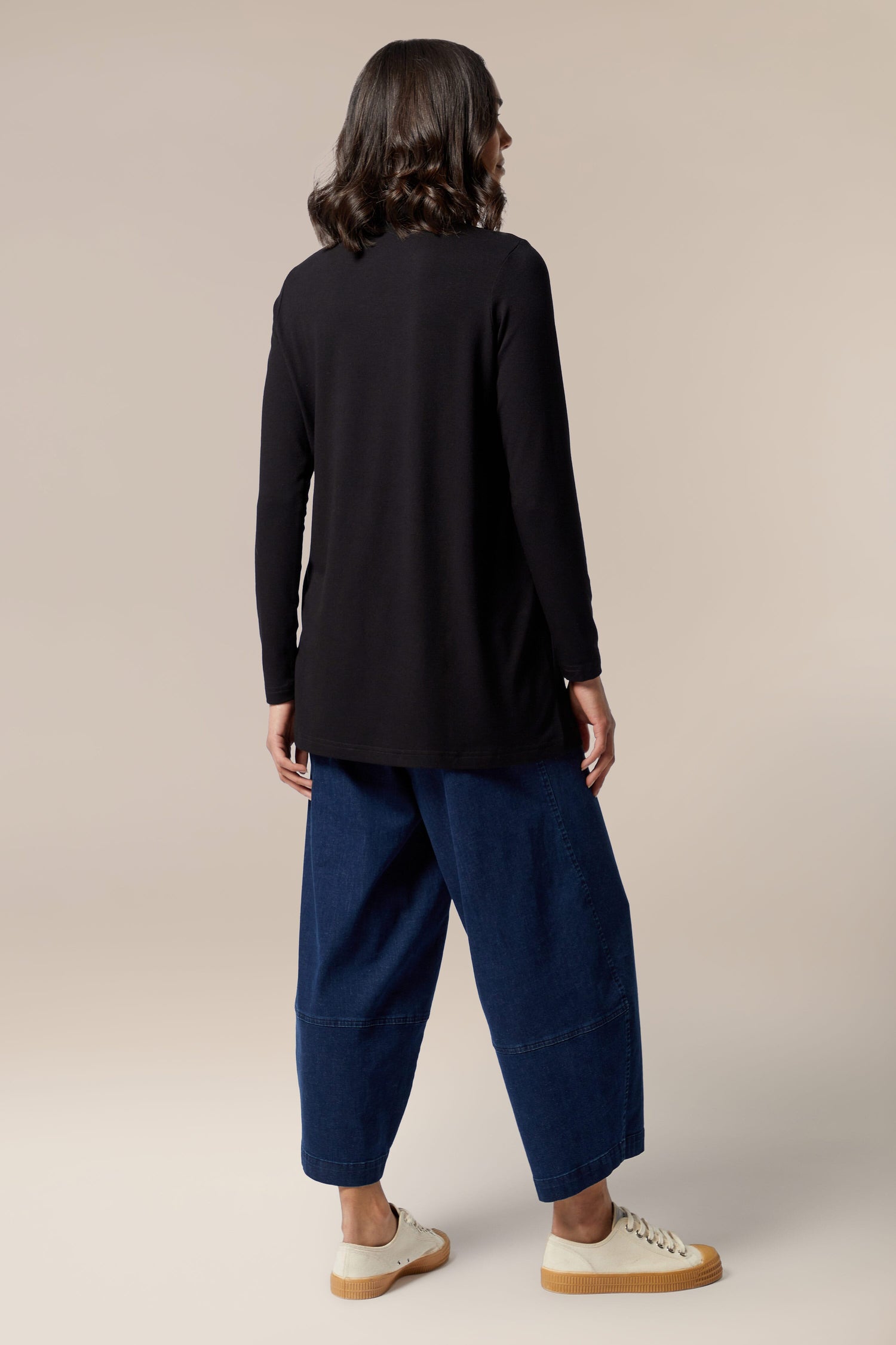 The back view of a woman wearing a black long sleeved Fluid Crepe Flared Polo Neck and blue wide leg pants.