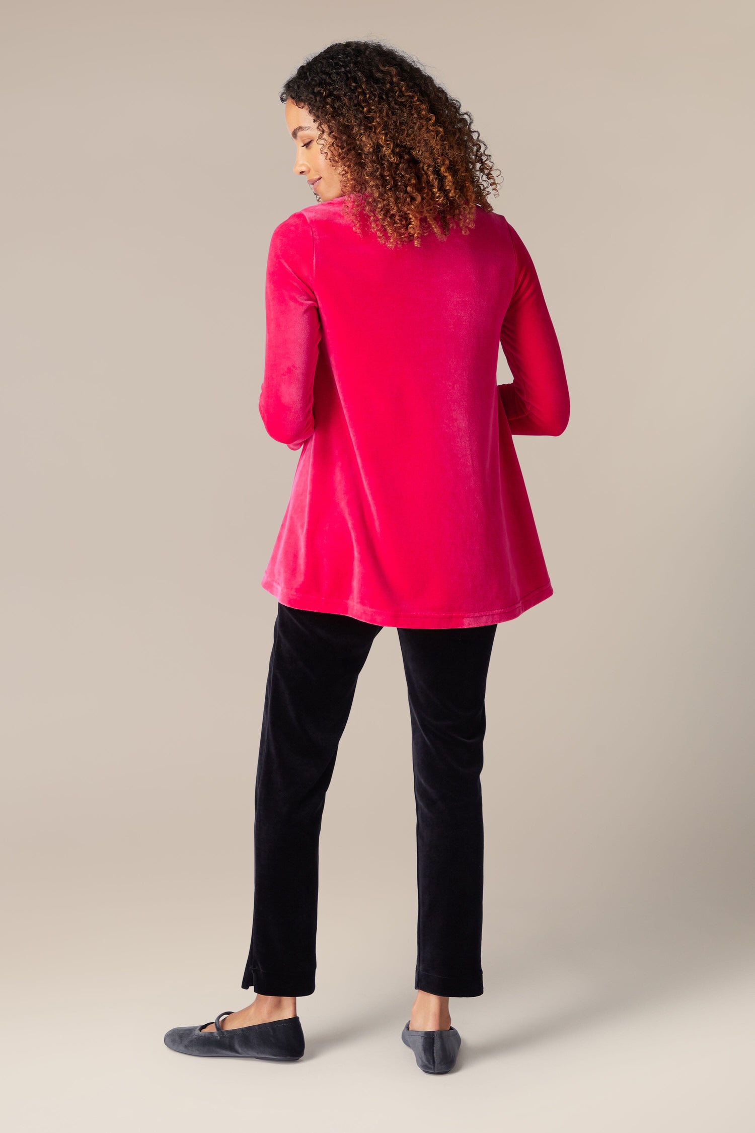 The luxurious back view of a woman wearing a pink Velvet Jersey Swing Top and elegant black pants.