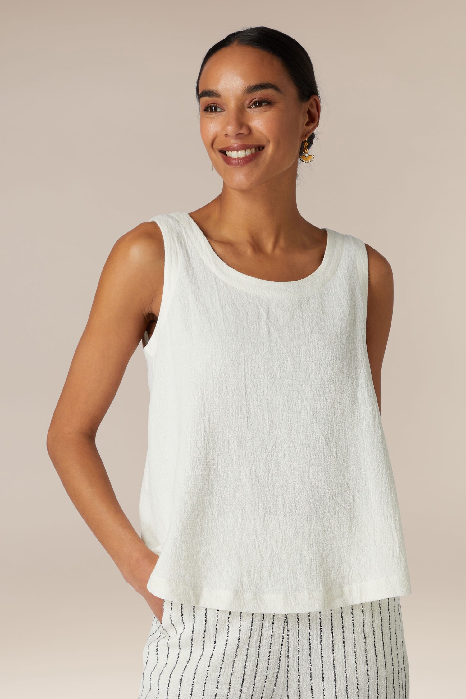 A woman in a Linen Viscose Vest and striped trousers smiles slightly while posing against a neutral background.