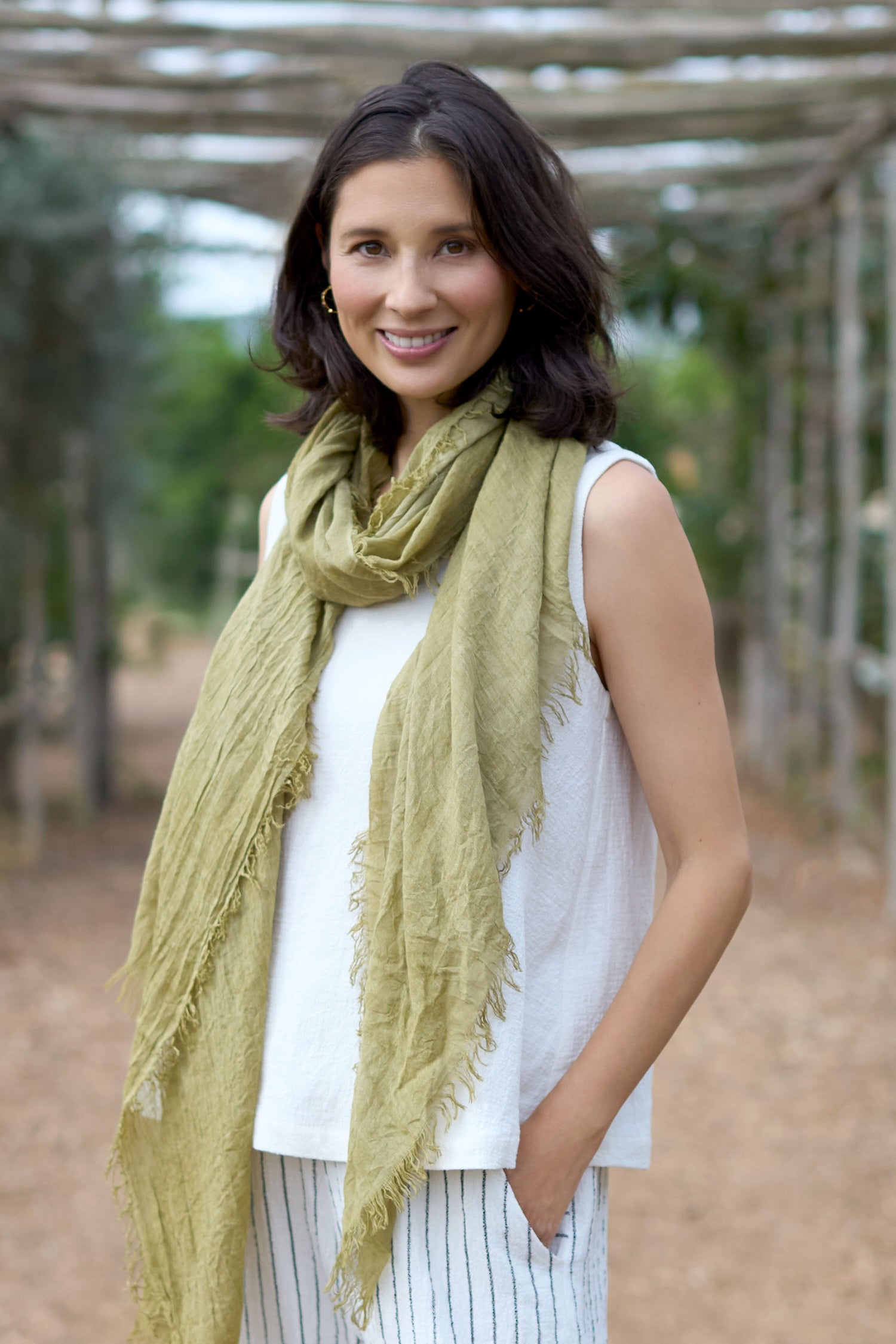 A woman stylishly coordinates her outfit with a green Linen Viscose Vest and striped pants.