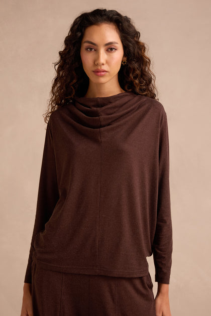 A person with long curly hair wearing the Soft Viscose Jersey Ruched Top in brown stands in front of a plain, light beige background.