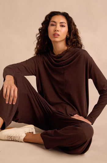 Woman with curly hair wearing the Soft Viscose Jersey Ruched Top lounge set in brown and white sneakers sits on the floor against a beige background.