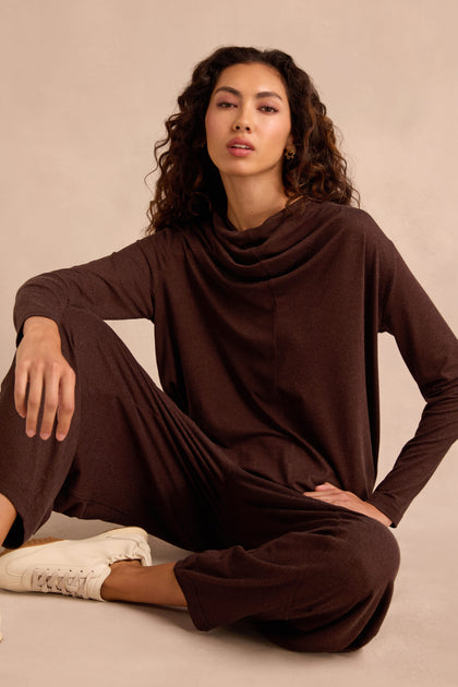 Woman with curly hair wearing the Soft Viscose Jersey Ruched Top lounge set in brown and white sneakers sits on the floor against a beige background.