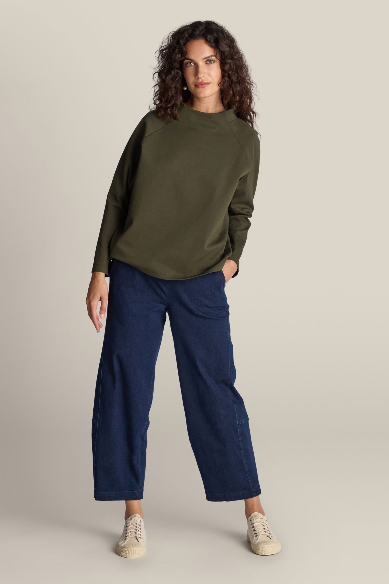 Person showcasing effortless style in a green Ponte Boxy Top, blue wide-leg jeans, and beige sneakers, standing against a light background.