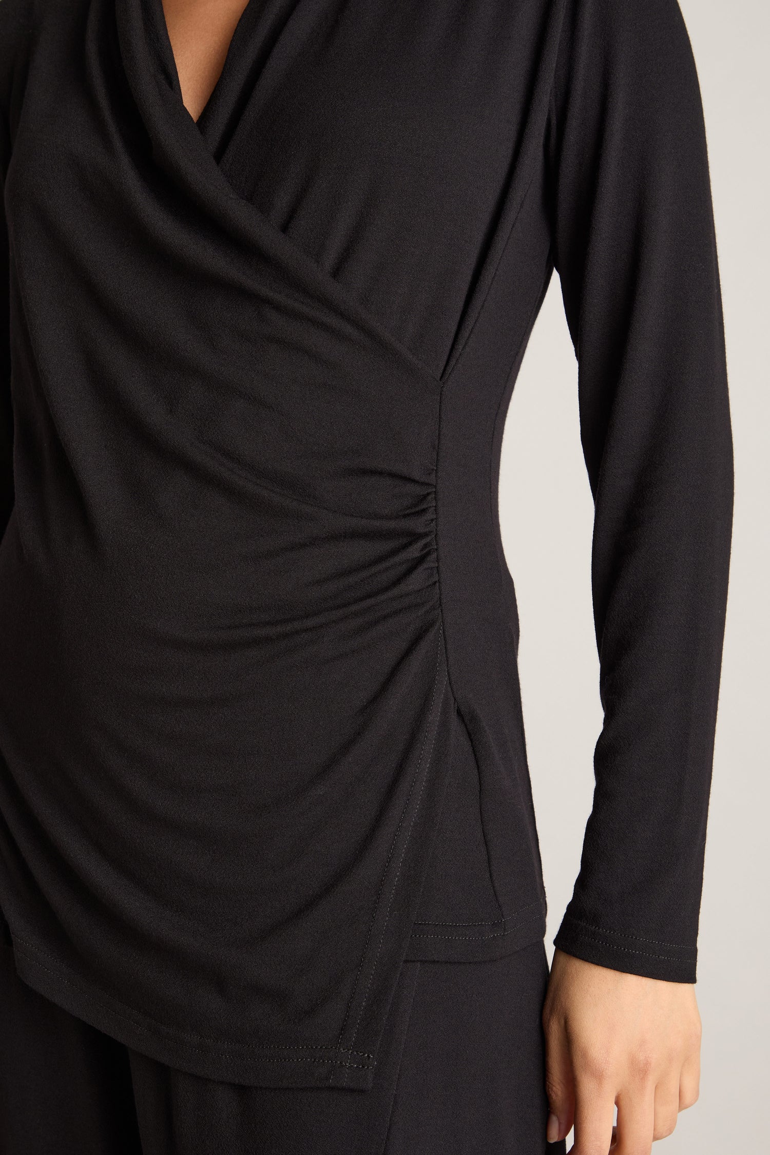 A person is wearing a Fluid Crepe Jersey Ruched Side Top in black, which features long sleeves and accentuates an hourglass silhouette.