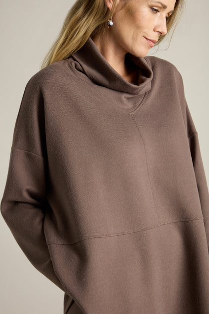 A person wearing a brown, long-sleeve Marl Jersey Sweatshirt featuring a diagonal marl knit pattern, looks downwards with hands in pockets.