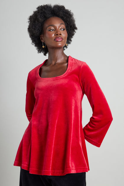 A person is wearing a Velvet Jersey Horseshoe Neck Top in red, featuring long sleeves and a chic neckline, standing against a plain background.