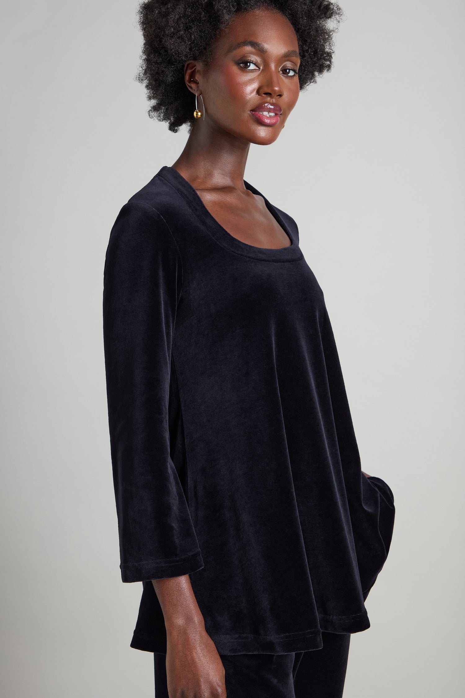 A person wearing the Velvet Jersey Horseshoe Neck Top in black, featuring flared sleeves and a loose fit, stands against a neutral background.