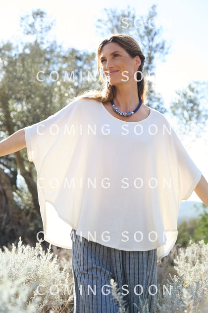 A woman in a linen viscose relaxed top and striped pants stands outdoors with arms open, wearing a blue SPT6223-IHL necklace. "Coming Soon" text overlaid.