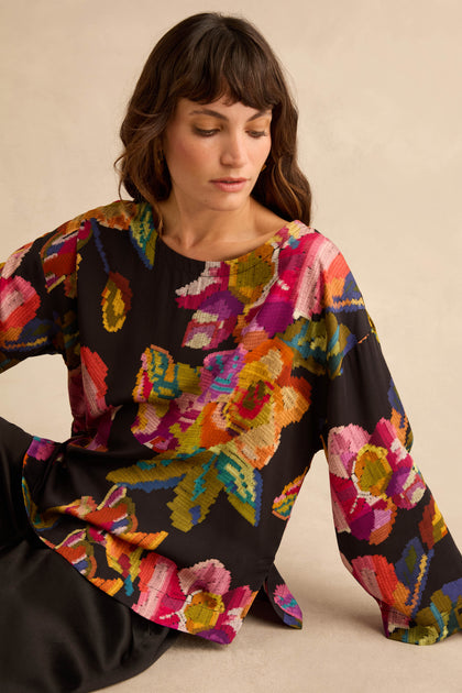 A person wears a Pixelated Floral Relaxed Top with long sleeves, a black background, and a relaxed-fit, pixelated floral print.