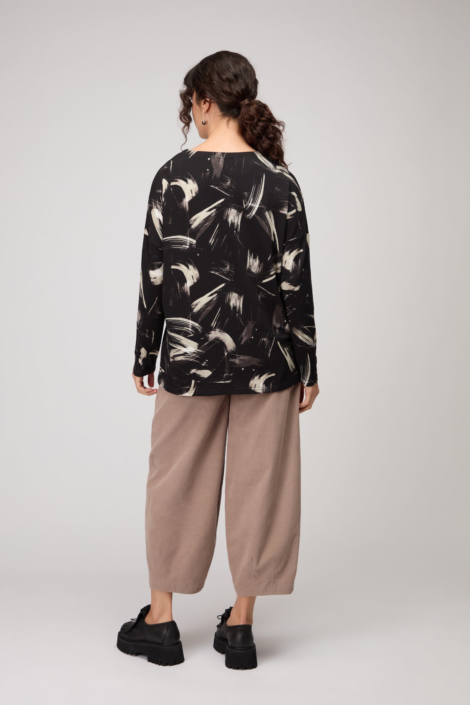 A person faces away, wearing the Painted Brushstrokes Jersey Top in black and white, paired with wide beige pants and black platform shoes, set against a neutral background.