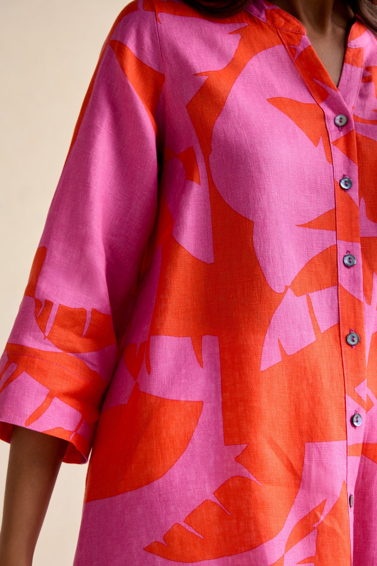 A close-up of a person wearing the Palm Mirage Linen Shirt—pink linen with bold red abstract tropical print, three-quarter sleeves, and a relaxed fit.