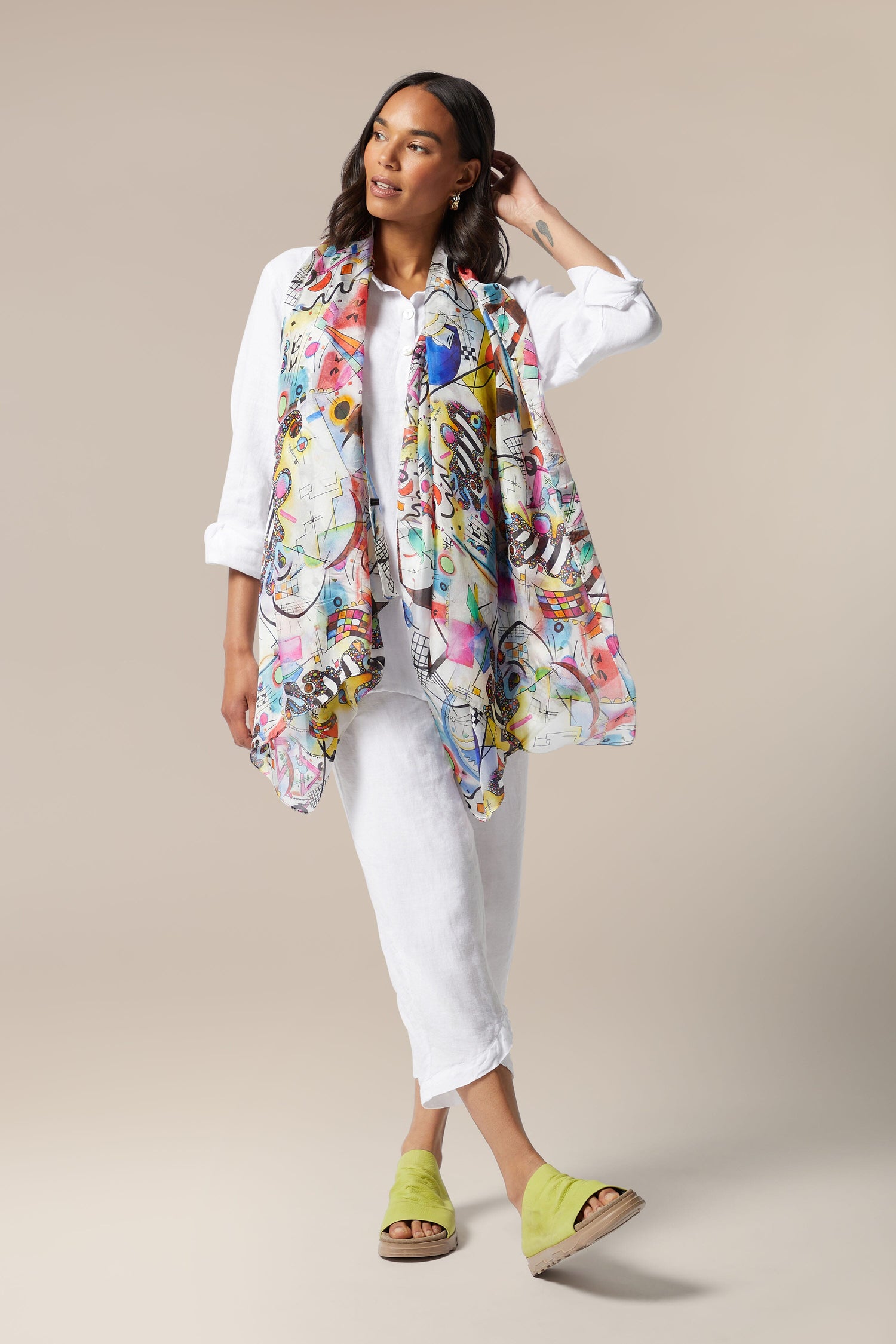 A woman wearing a Cubist Silk Scarf and white pants.