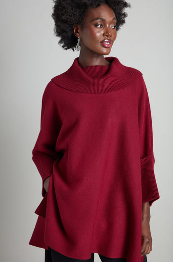 A person wearing a red, oversized Roll Neck Knit poses in front of a neutral background, showcasing perfect layering for cozy comfort.