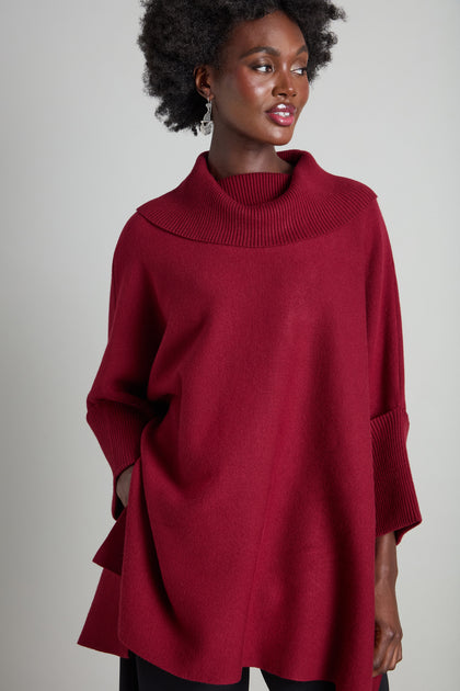 A person wearing a red, oversized Roll Neck Knit poses in front of a neutral background, showcasing perfect layering for cozy comfort.