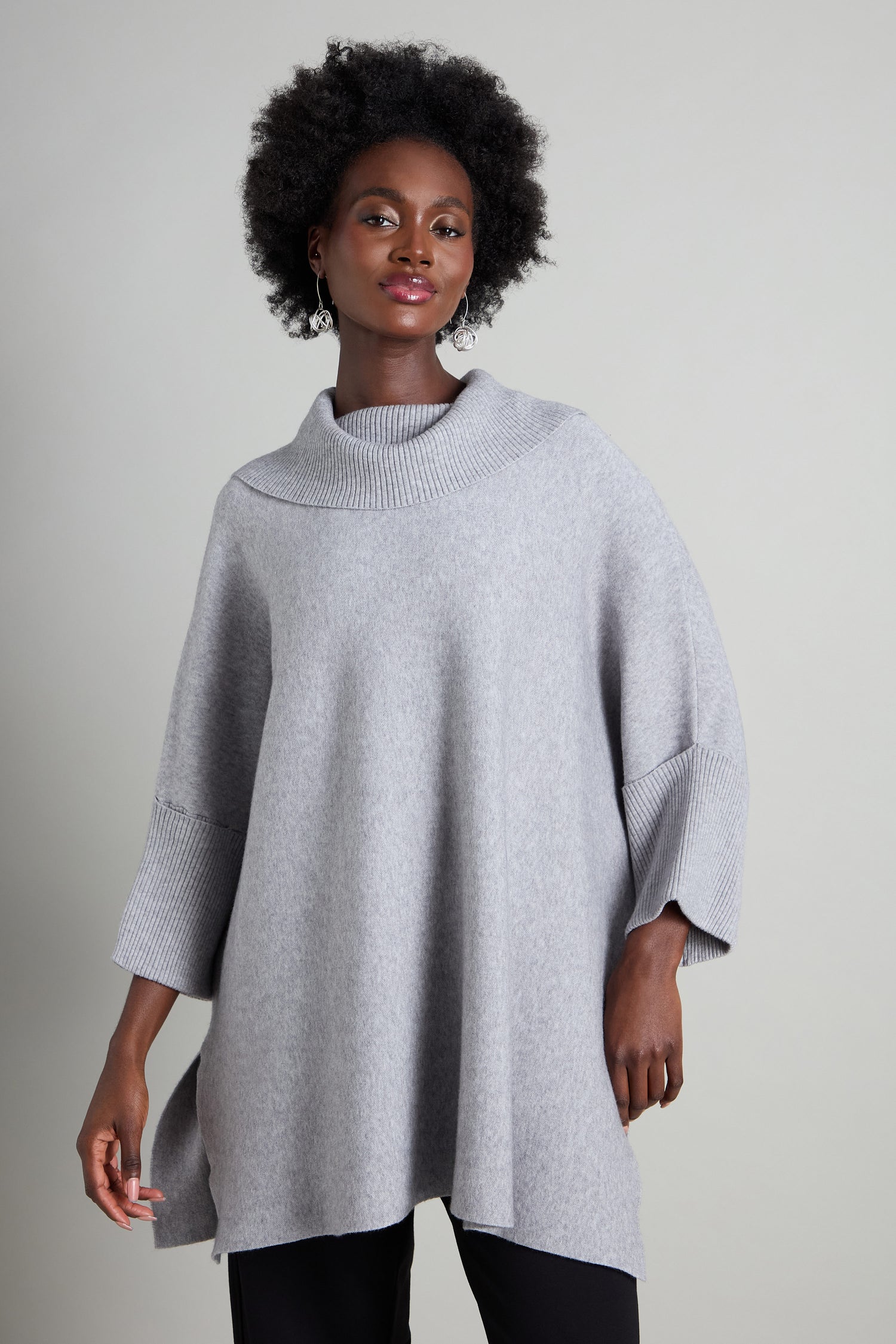 A person wearing a gray Roll Neck Knit sweater with an oversized and cozy design stands against a plain background.