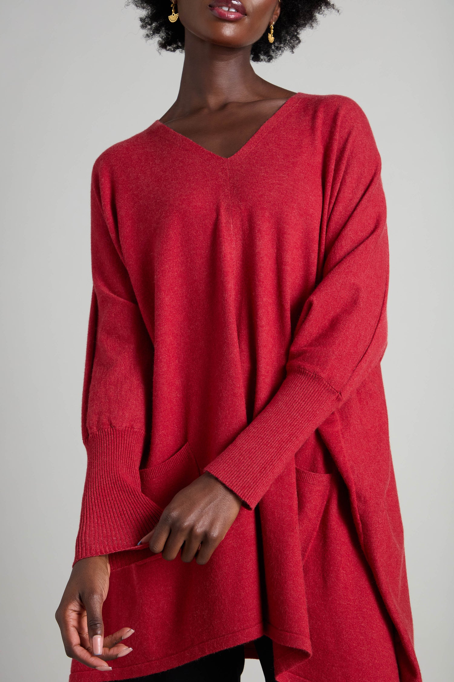 A person wearing a V Neck Knit in red, featuring pockets and ideal for layering during the cooler months, stands against a plain background.