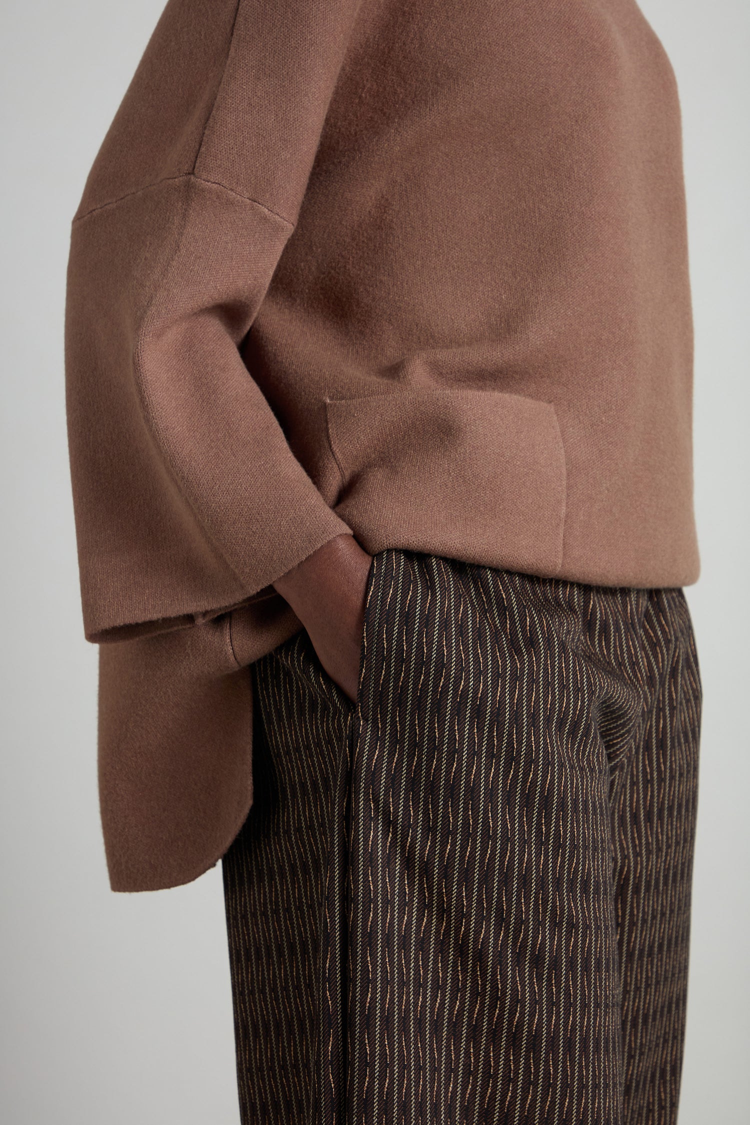 A person stands confidently with one hand in their pocket, showcasing a brown oversized sweater with pocket detail and stylish Mini Check Jersey Bubble Trouser.