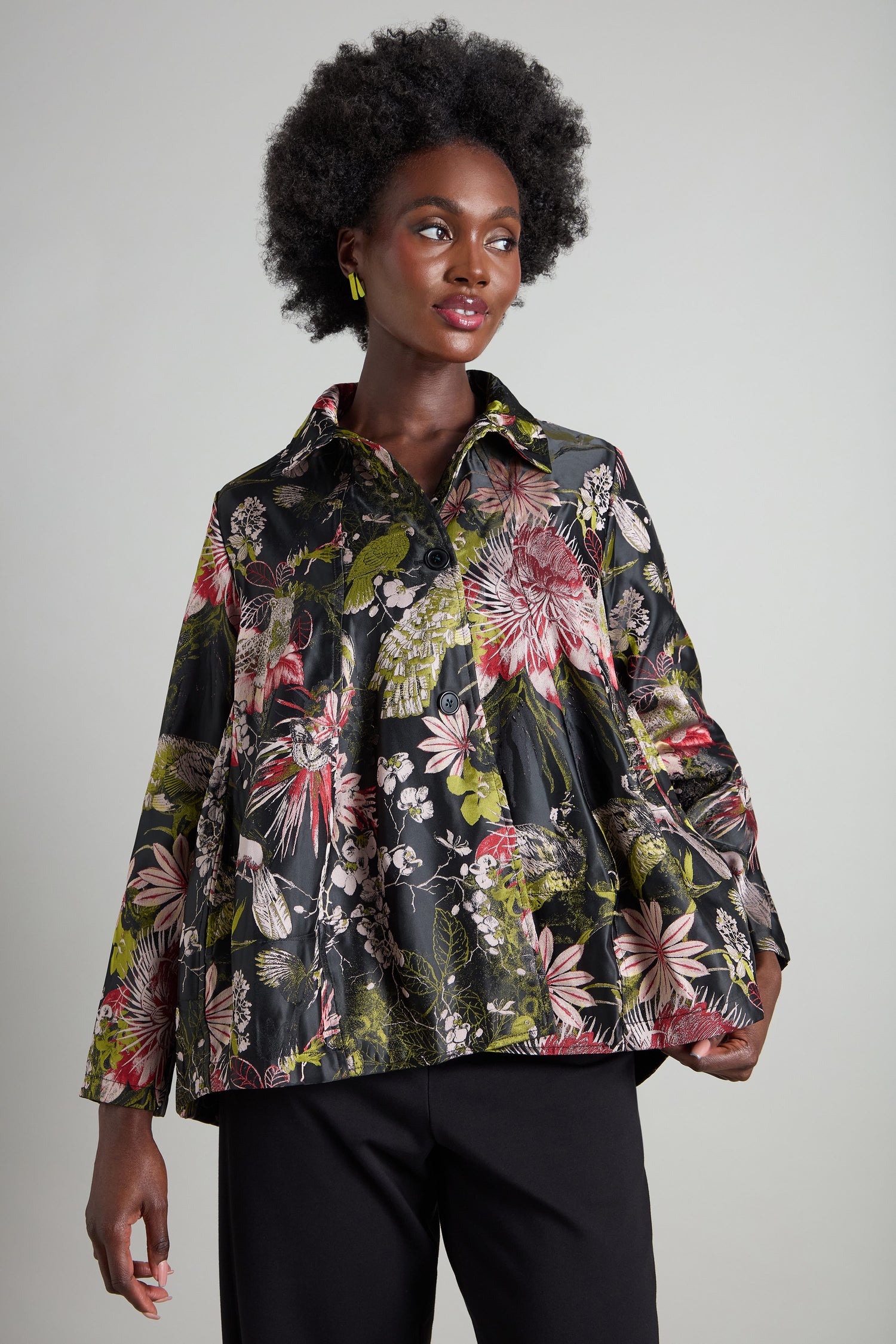 A person stands against a plain background wearing the Jacquard Floral Jacket, featuring a classic collared design. Its graceful patterns capture the essence of an Oriental garden, bringing an air of sophistication to any environment.