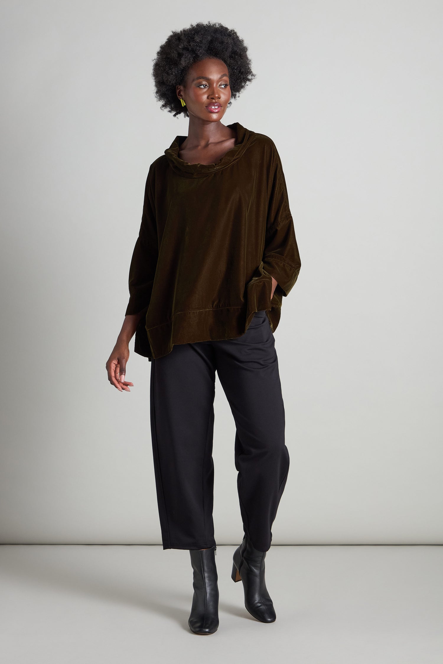 Against a plain background, a person with curly hair strikes a pose wearing the Cowl Neck Boxy Top, paired with black pants and boots. This stylish outfit features 3/4 length flared sleeves.