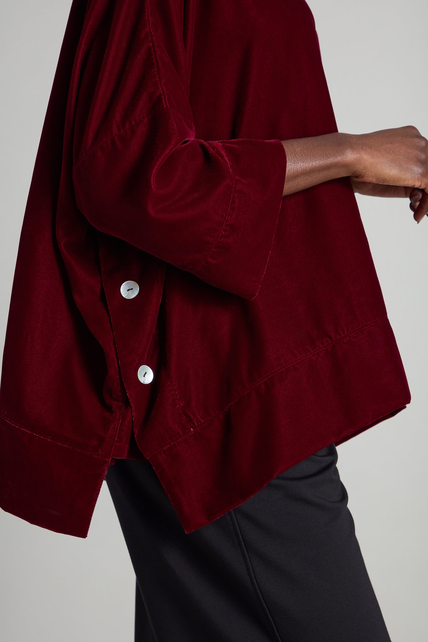 A person is wearing the Cowl Neck Boxy Top, featuring dark red velvet, 3/4 length flared sleeves, and shell button-up detailing, beautifully paired with sleek black pants.