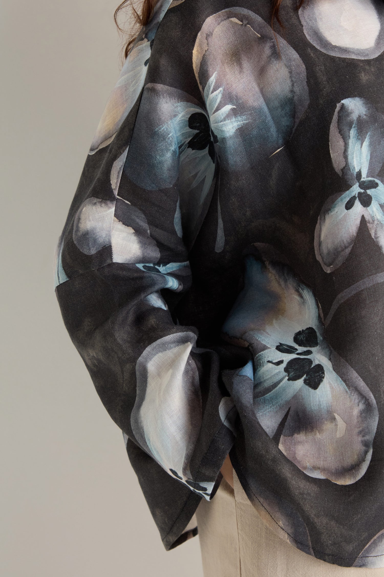 A person is seen from the back and side wearing the Abstract Floral Linen Shirt, a dark relaxed-fit linen top featuring bold blue and white abstract floral patterns.