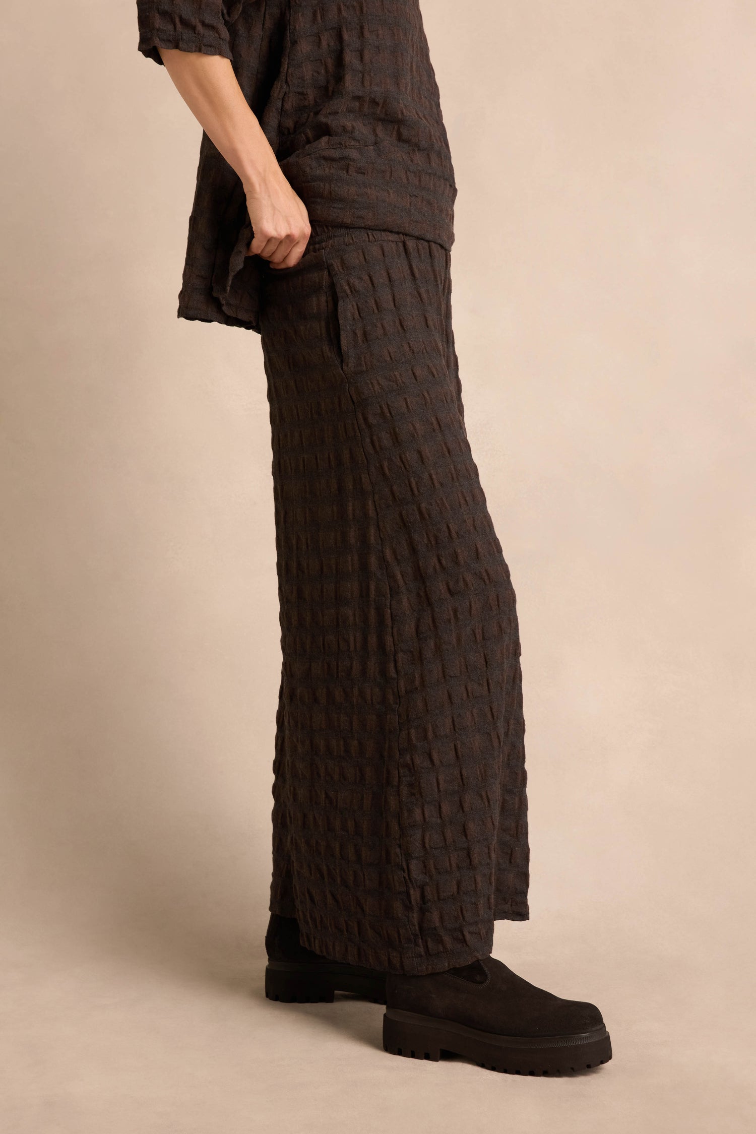 Wearing the Chocolate Waffle Check Wide Trousers as part of a textured dark brown matching set with wide-leg pants and a long top, paired with chunky black shoes against a neutral background.