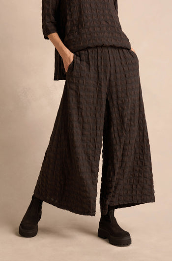 A person wearing Chocolate Waffle Check Wide Trousers and a matching textured top, with hands in pockets and paired with black boots against a neutral background.