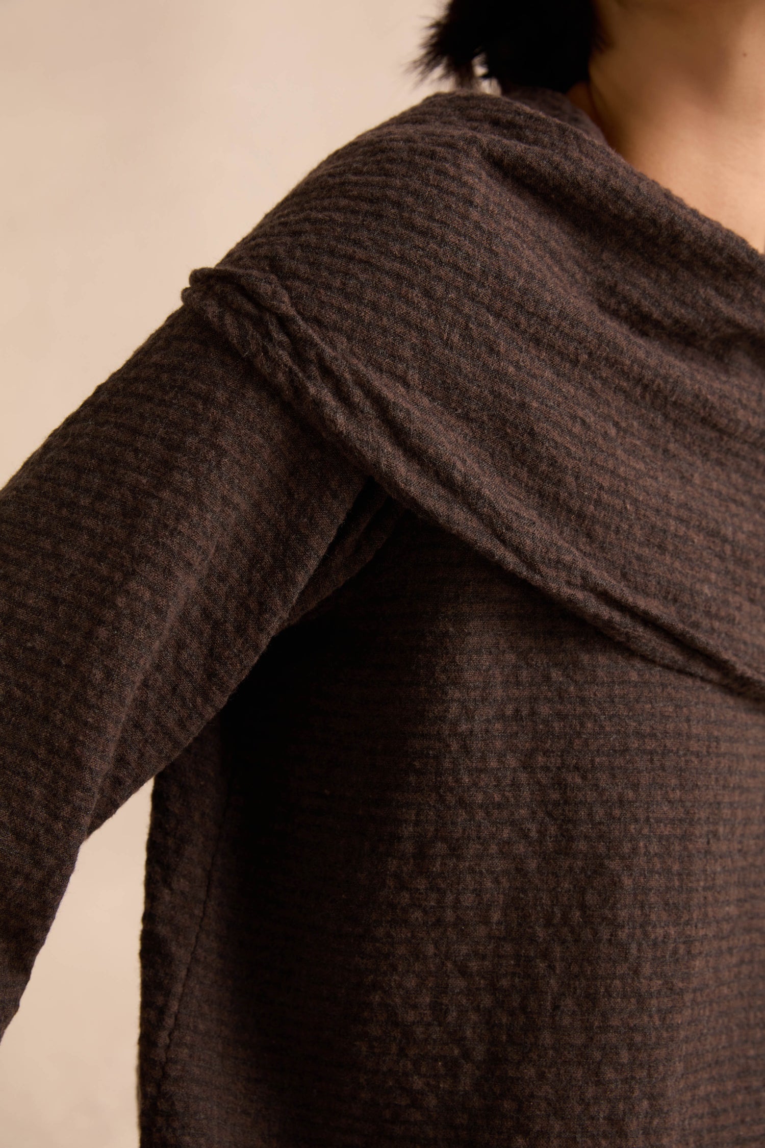 Close-up of a person wearing the Chocolate Draped Neck Top, featuring a textured dark brown knit with a wide, asymmetric draped neckline, shown from shoulder to upper chest against a neutral background.