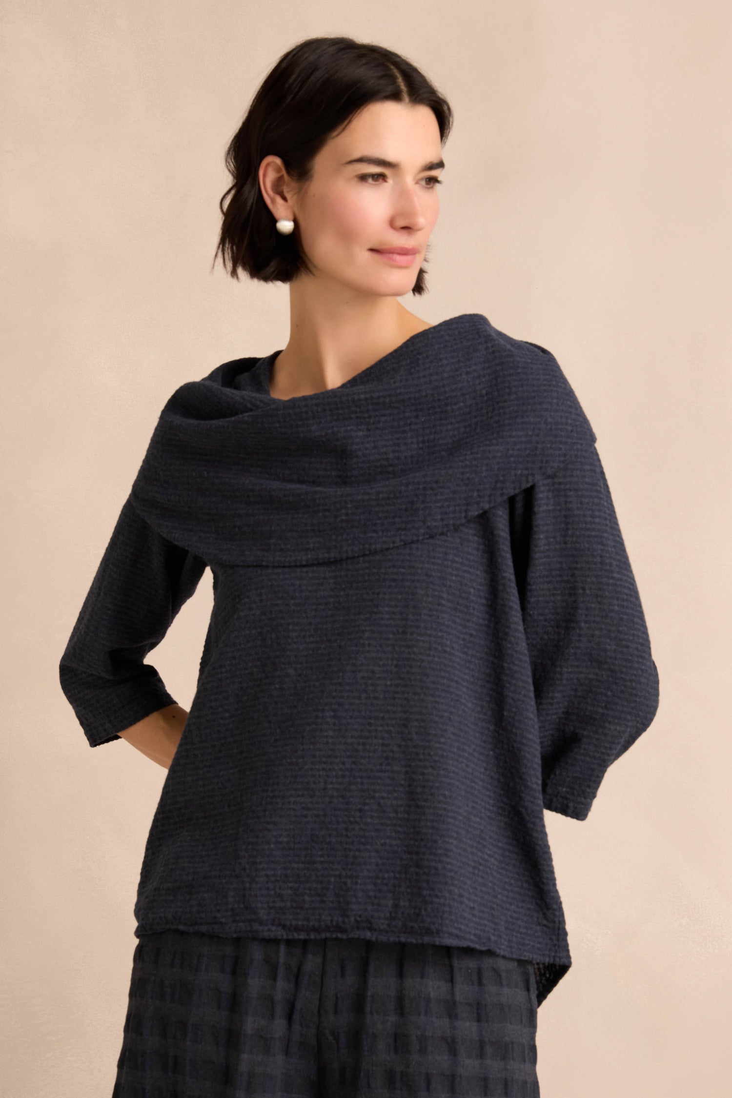A woman models the Navy Draped Neck Top, featuring a wide cowl neck, three-quarter sleeves, and a textured design. Crafted from soft cotton-viscose jersey for a relaxed fit, she stands against a neutral background.