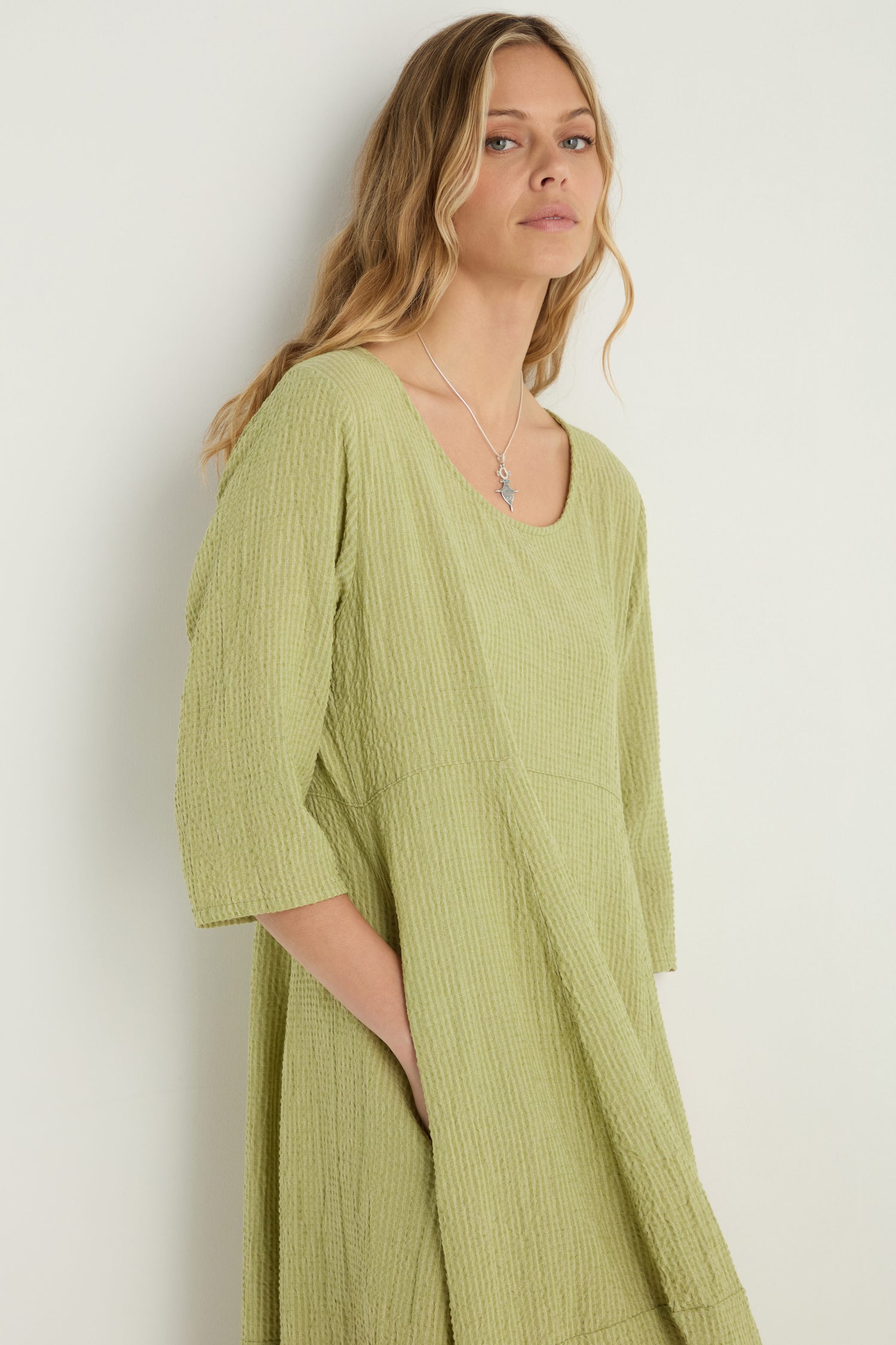 A woman with long, wavy blonde hair models the Crinkle Bubble Dress in light green, featuring three-quarter sleeves, against a plain light background.