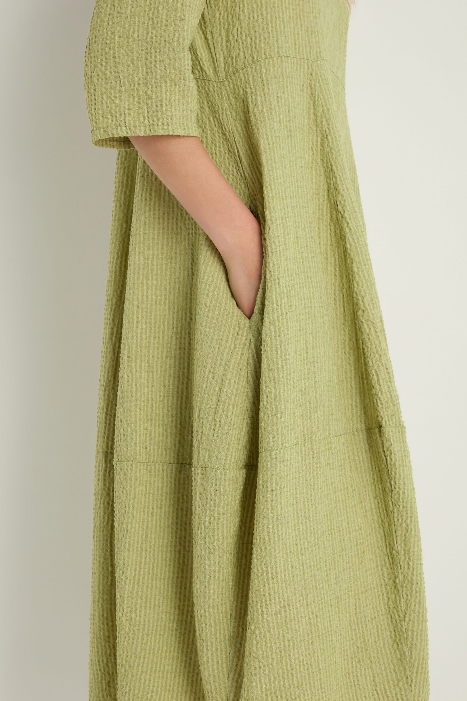 A person in the Crinkle Bubble Dress—a relaxed-fit, textured light green cotton blend with side pockets—stands from shoulder to mid-calf against a plain background.