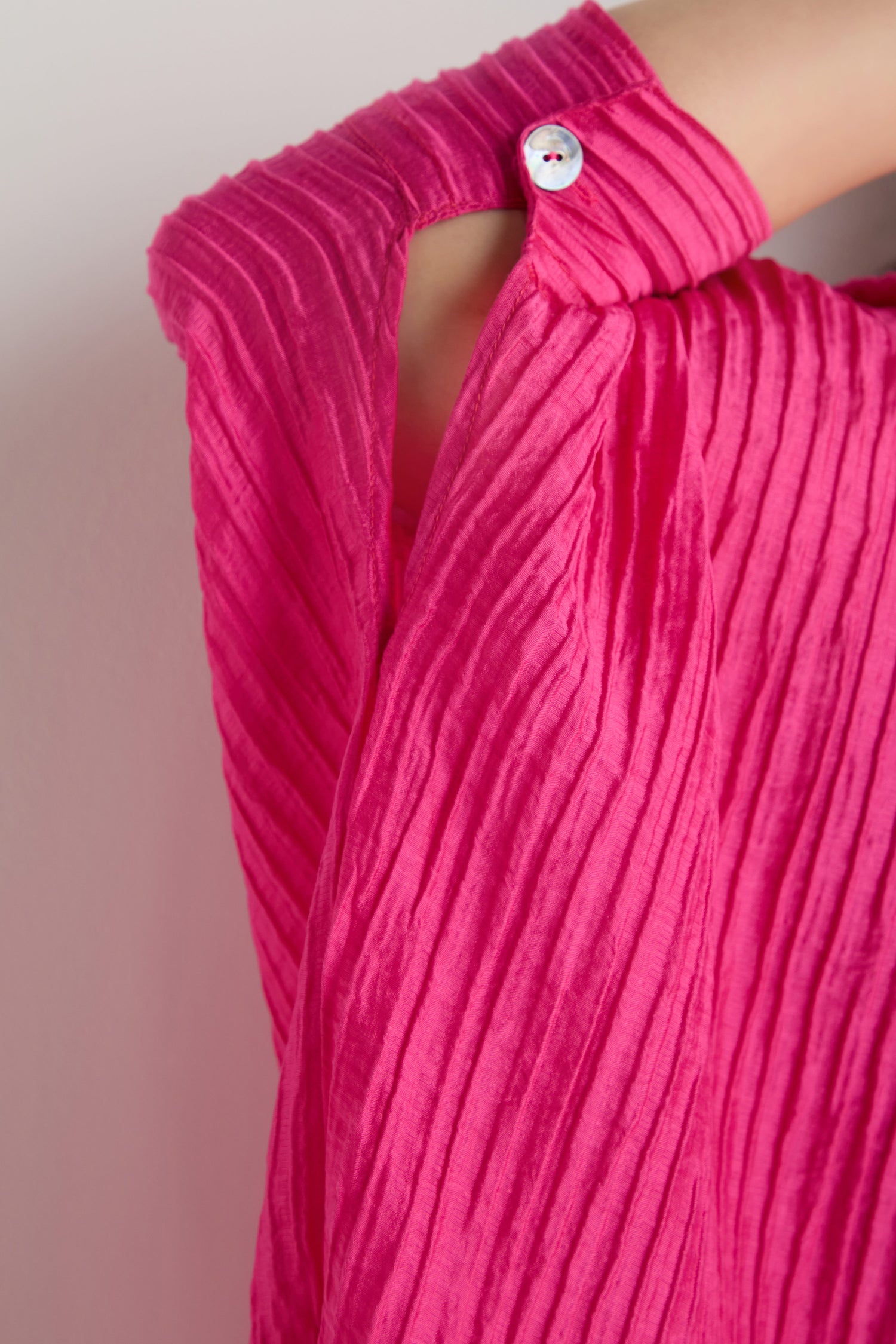 Close-up of a person wearing the Pleated Easy Shirt in bright pink, featuring pleats and a white button fastening near the shoulder.