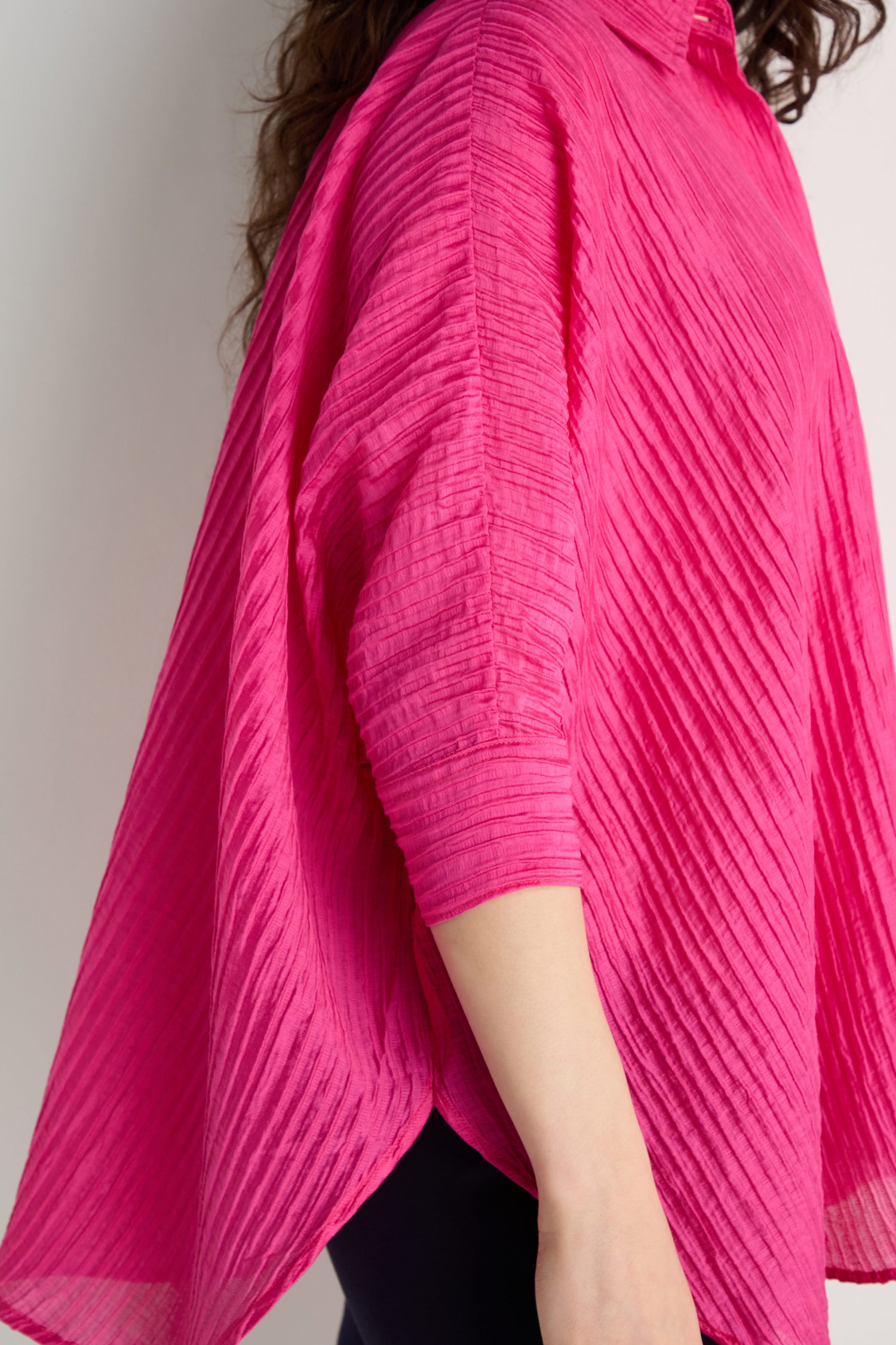 A person wearing the Pleated Easy Shirt, featuring a textured, oversized bright pink design with three-quarter sleeves, stands against a light background.