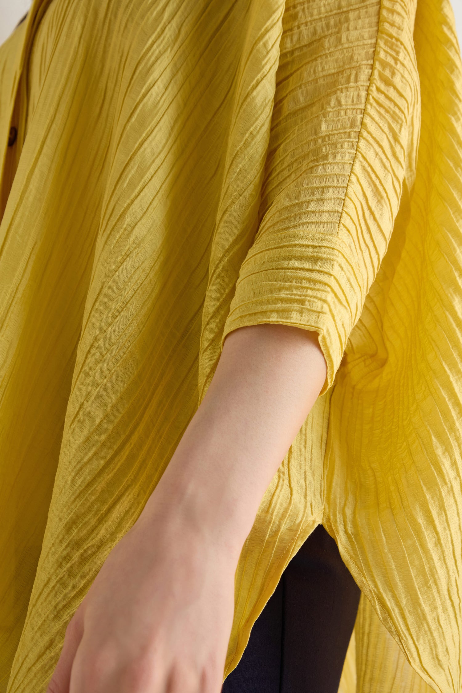 Close-up of a person wearing the Pleated Easy Shirt in yellow, featuring a pleated texture and long sleeves, with a hand visible in the foreground.