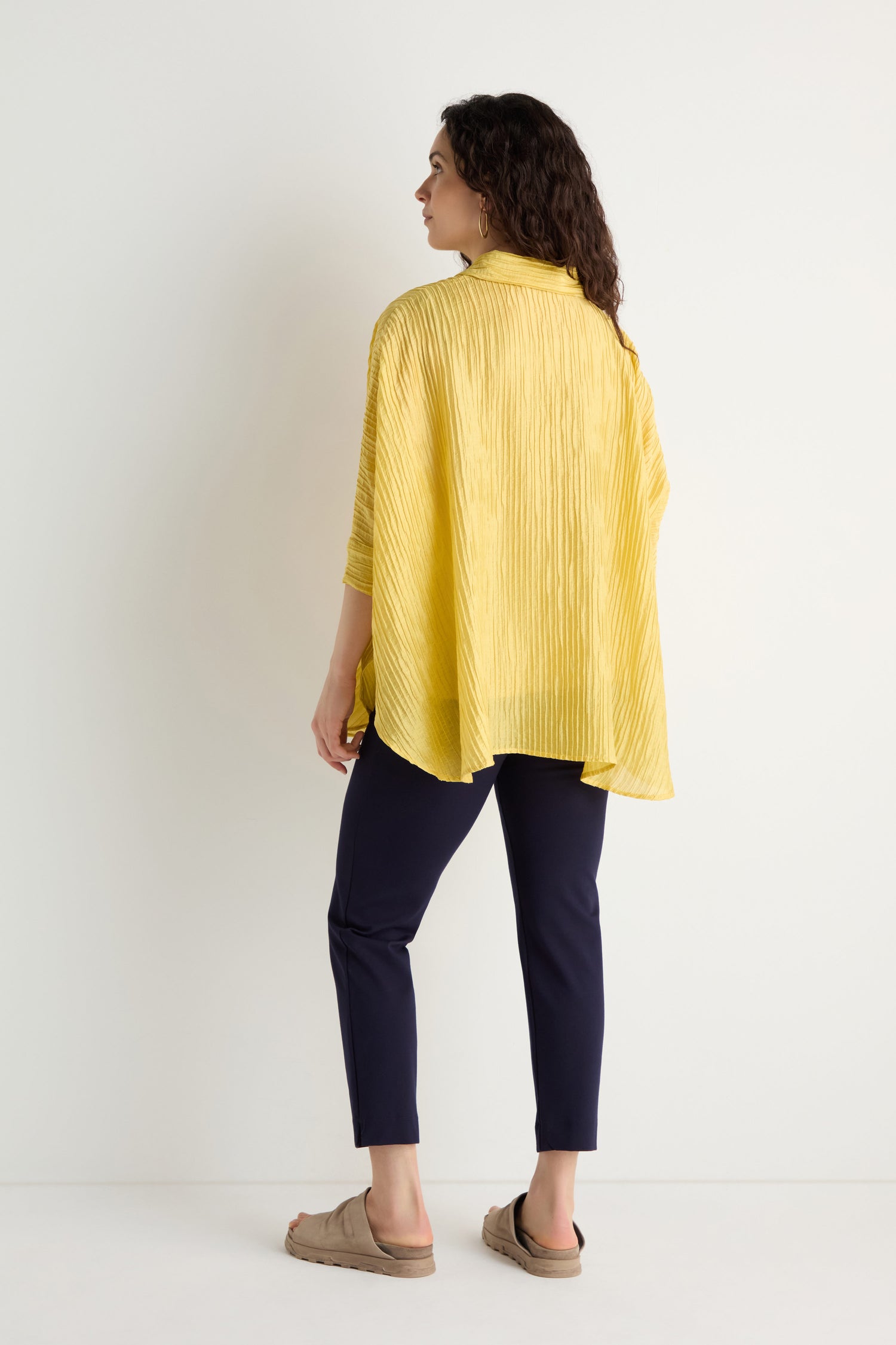 Person standing with back to camera, wearing the Pleated Easy Shirt in yellow, navy pants, and beige slip-on shoes against a plain white background.