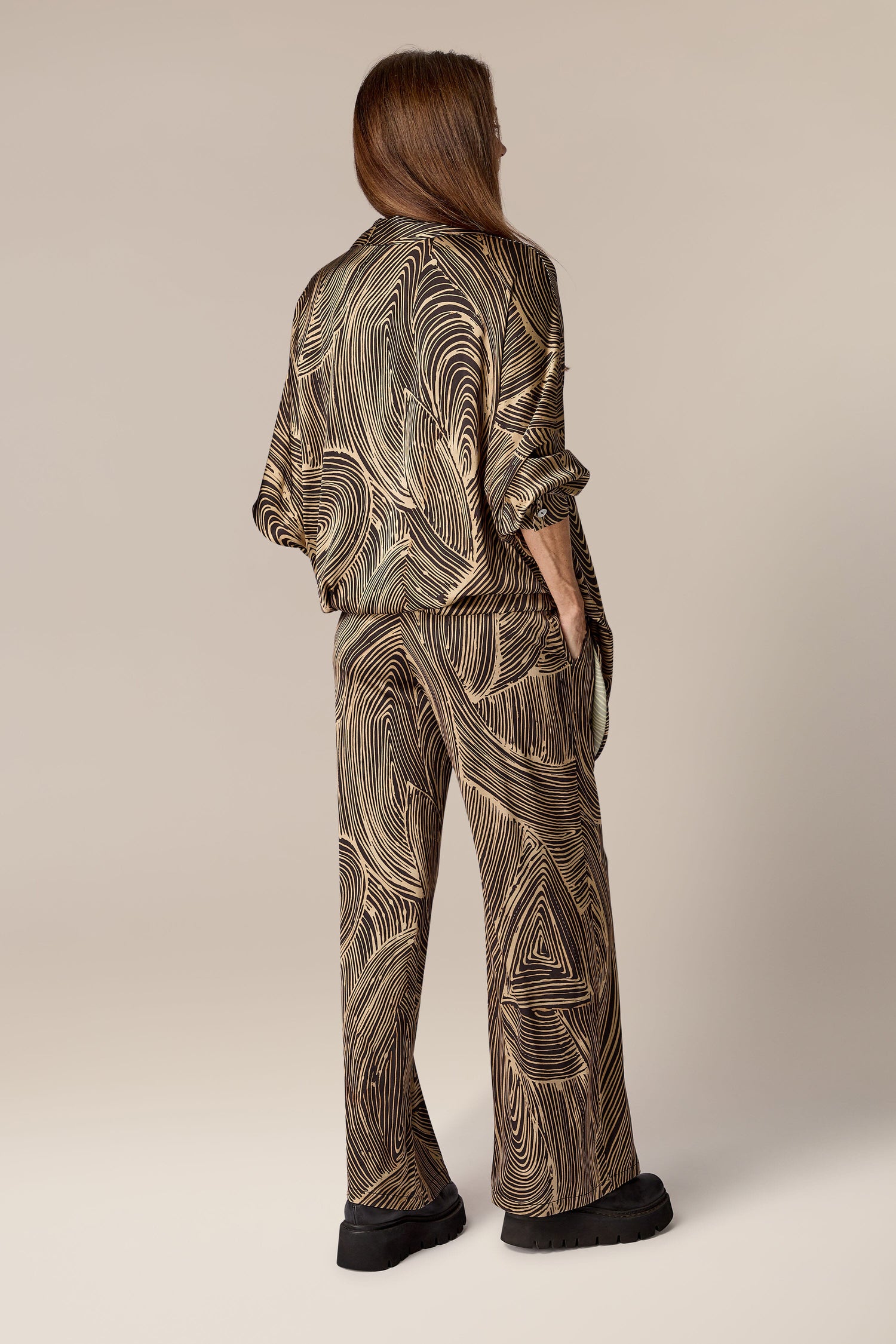 The back view of a woman wearing Swirl Pant, a contemporary design black and brown marble print jacket and pants.