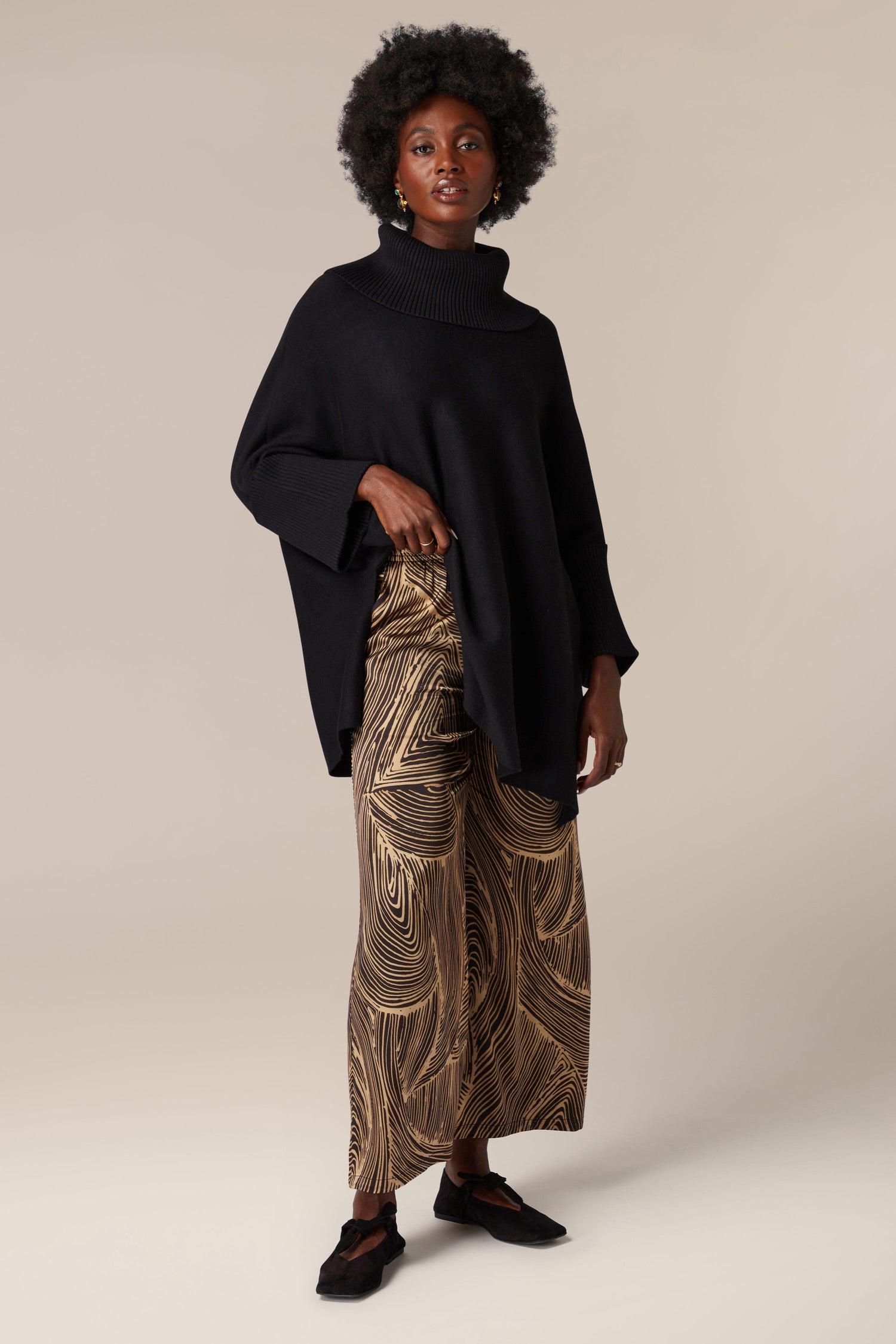 A woman showcasing artisanal flair in her contemporary black poncho and Swirl Trouser ensemble.