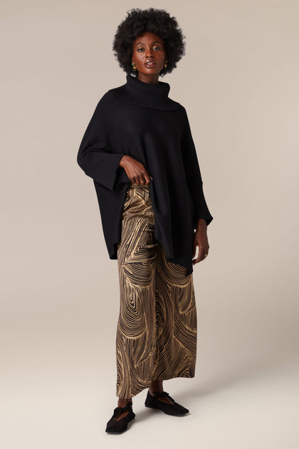 A woman showcasing artisanal flair in her contemporary black poncho and Swirl Trouser ensemble.