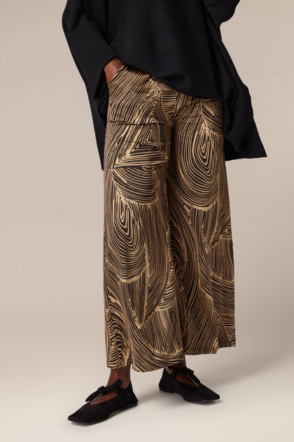 A woman in a black top and Swirl Trouser emanates contemporary design with artisanal flair.