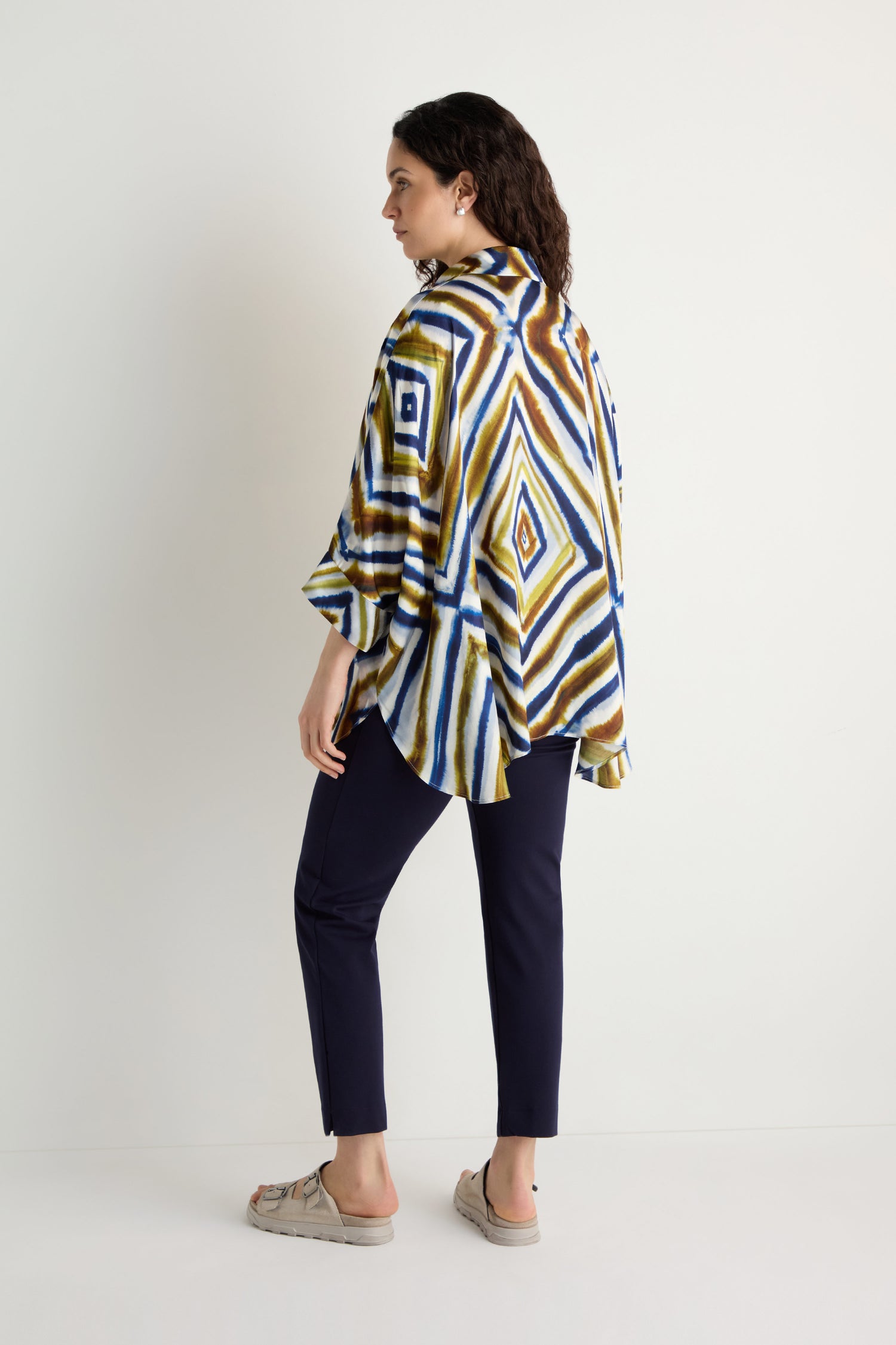 A woman stands sideways wearing the Wavy Lines Print Shirt, dark pants, and beige sandals, set against a plain white background.