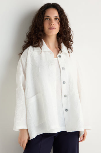 A woman with long curly hair wears the Pleated Leaf Short Jacket in white with dark pants, standing against a plain light background.