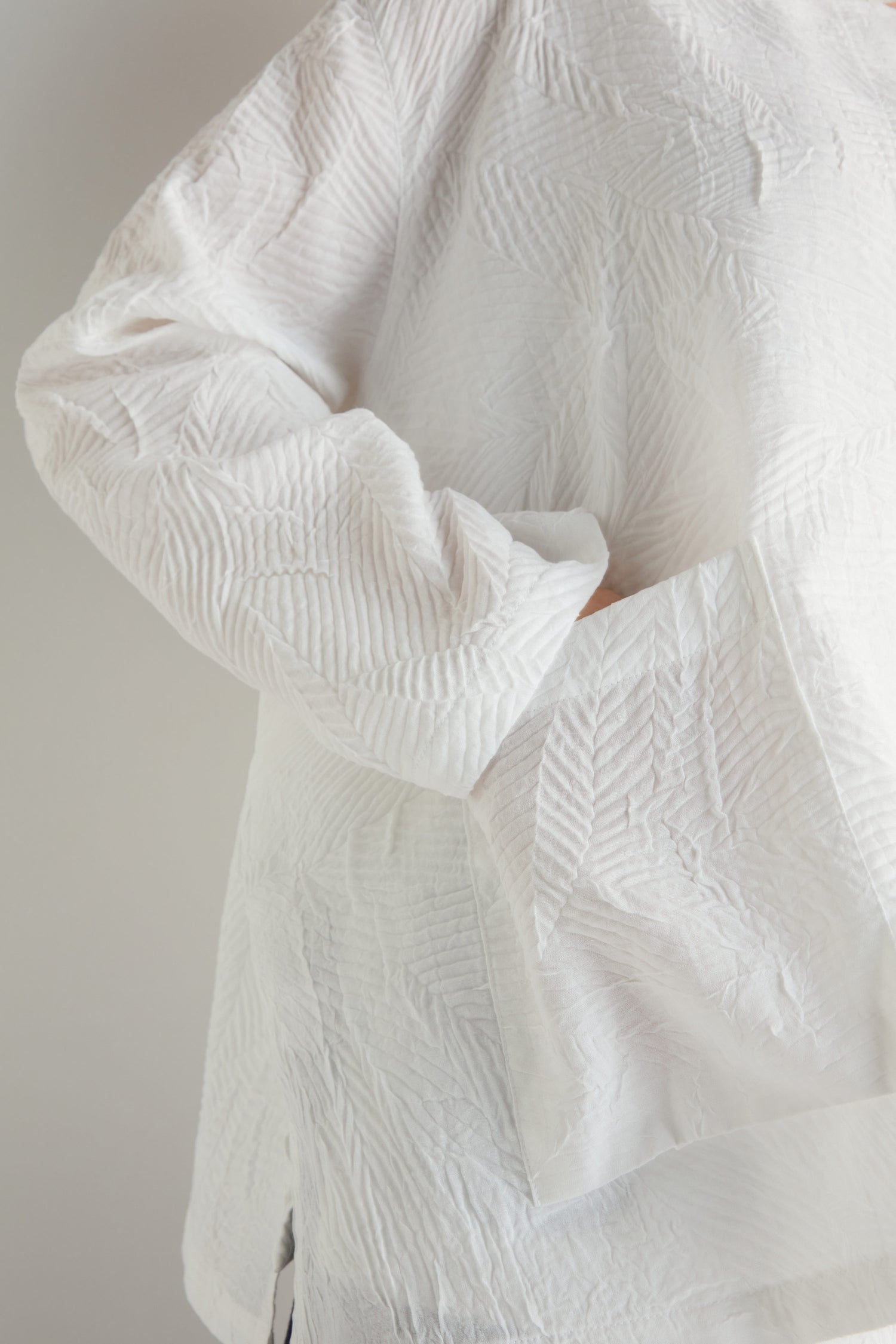 Model wearing the Pleated Leaf Short Jacket with hand partly tucked into the large front pocket; only torso and arm are shown.