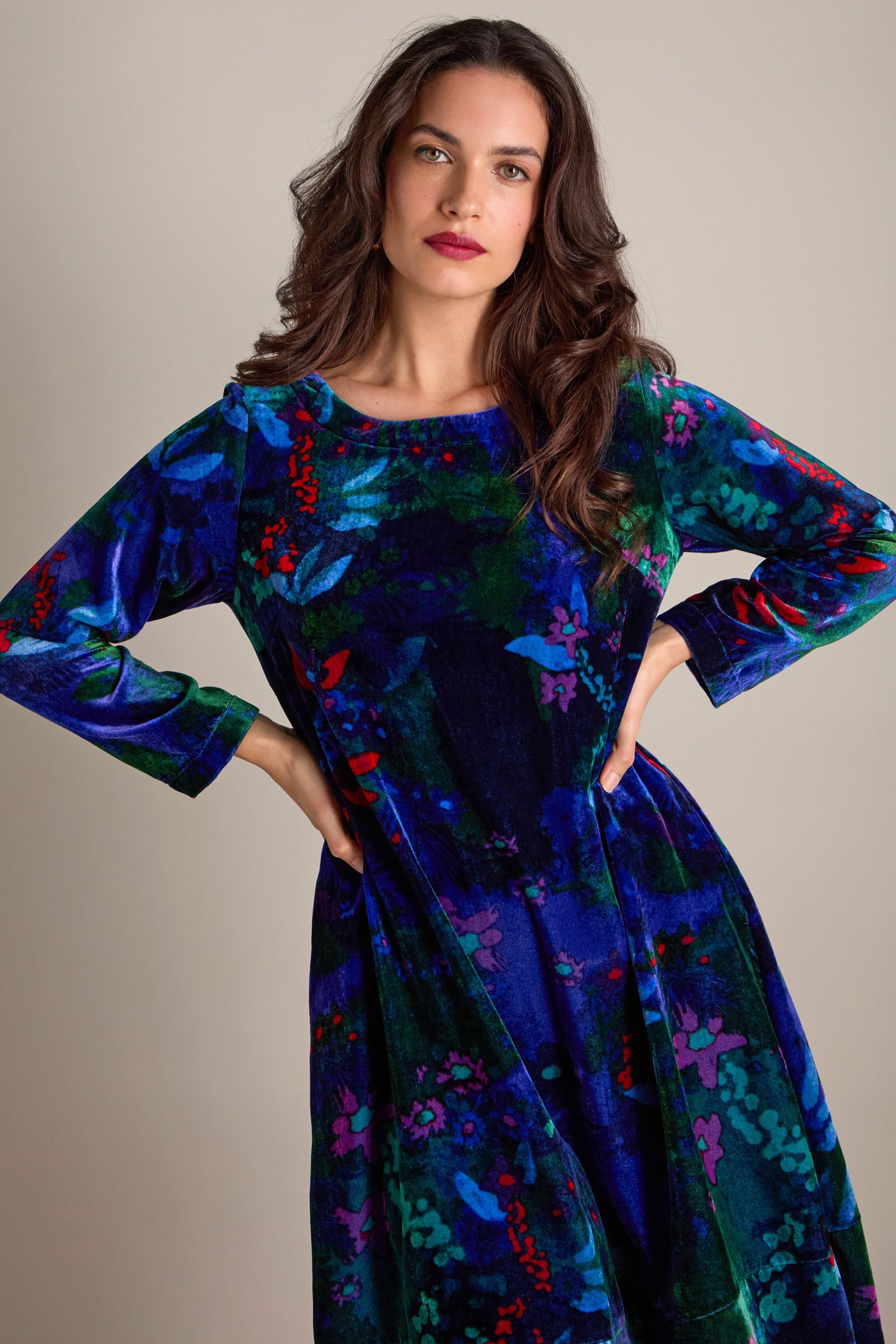 Dressed in the Late Night Flora Velvet Bubble Dress featuring a vibrant floral print, long sleeves, and a round neckline, a woman stands confidently with hands on hips, poised for evening events against a plain backdrop.